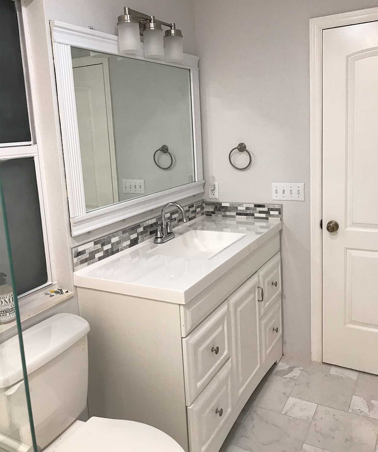 Mid-size white master bathroom with new mirror, vanity, and paint.